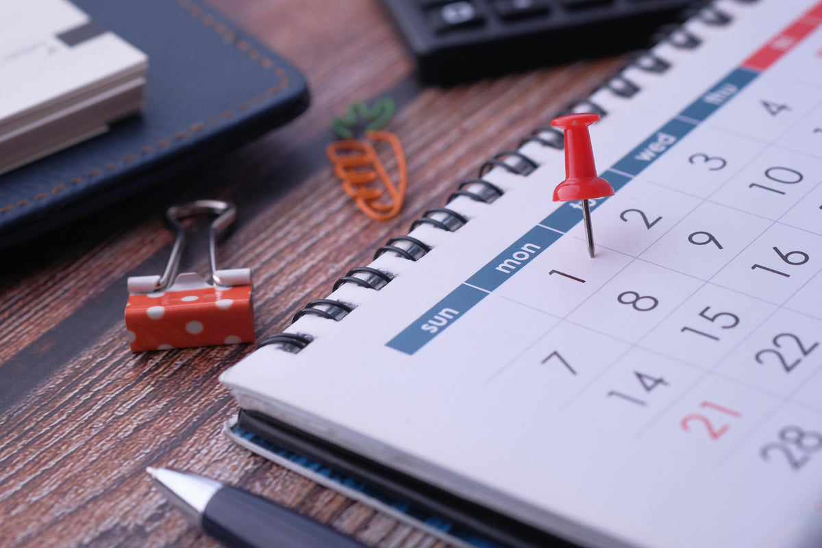 Calendar with red push pin on a wooden desk with office supplies